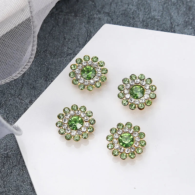 A collection of five green and clear rhinestone flowers on a white surface.