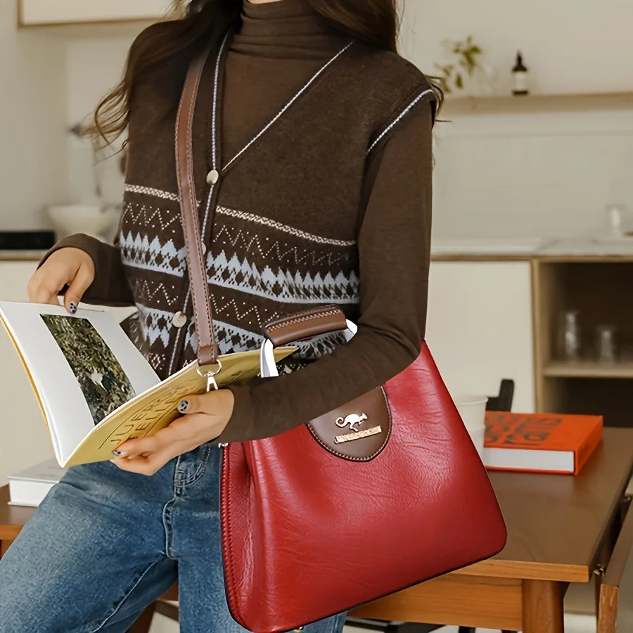 A woman holds a red leather crossbody tote bag and a yellow notebook while wearing a brown turtleneck sweater.