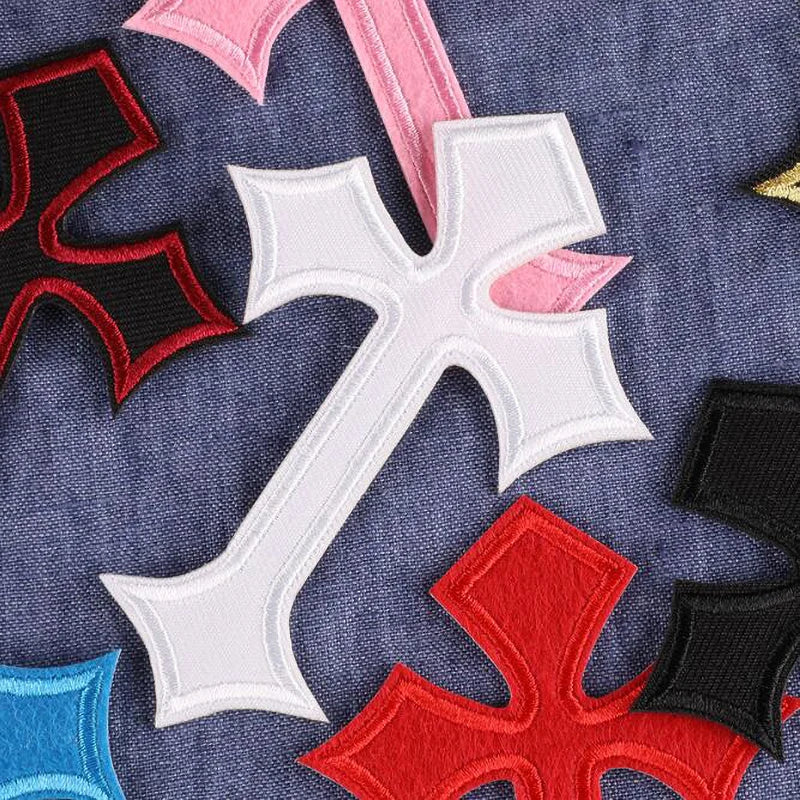 A collection of vibrant embroidered cross patches in red, pink, and white on a dark blue fabric background.