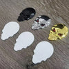Three skull emblems in black, silver, and gold chrome finish displayed on a gray wooden surface.