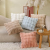 A collection of soft plush decorative pillows in cream, beige, light blue, and pink resting on a light-colored sofa.