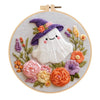 A cross stitch kit featuring a purple hat and floral embroidery on a light background.