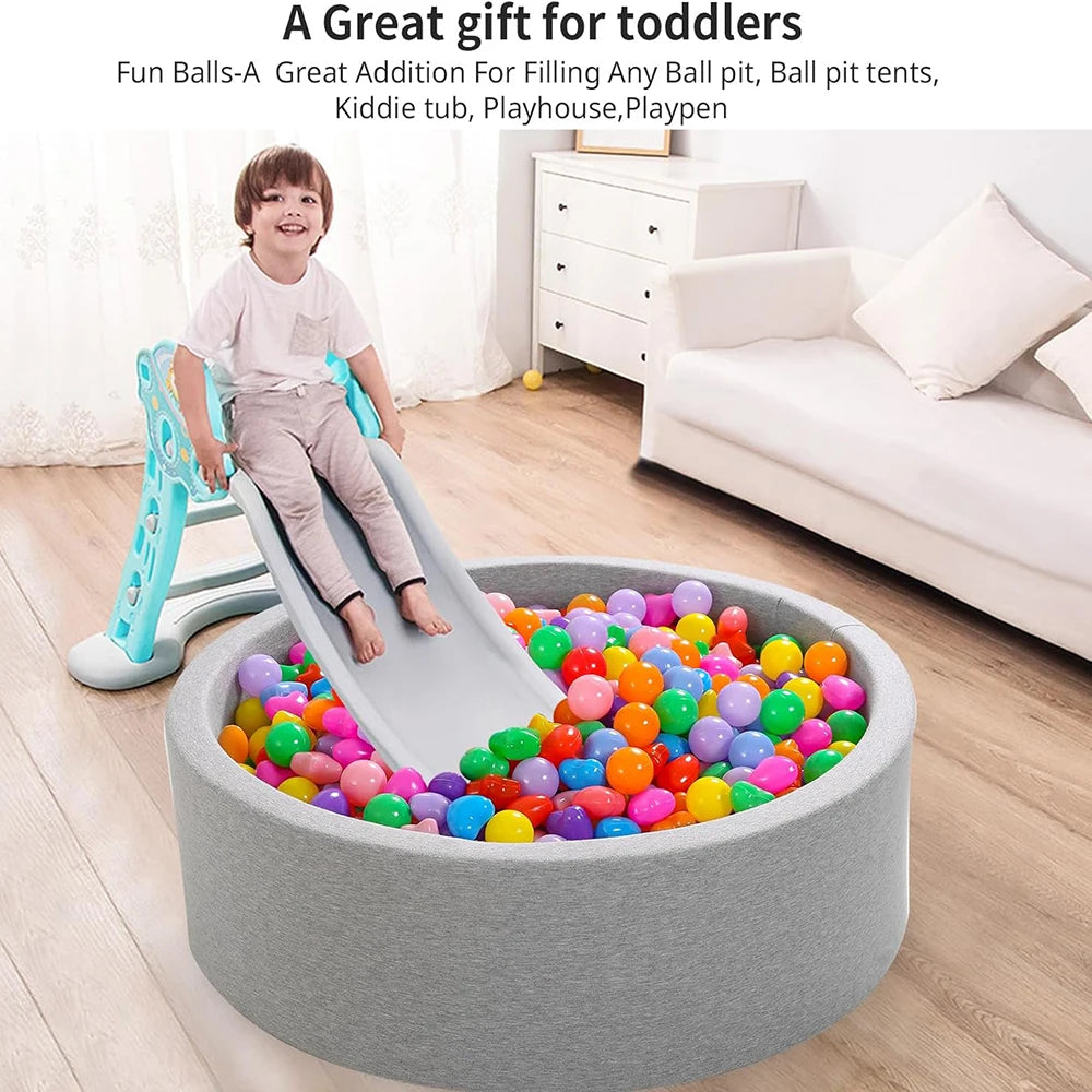 A plastic slide toy is positioned next to a large gray bowl filled with colorful non-toxic ball pit balls for toddlers.