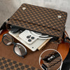 A brown Gucci print crossbody bag is open, revealing a smartphone and sunglasses on a wooden surface.