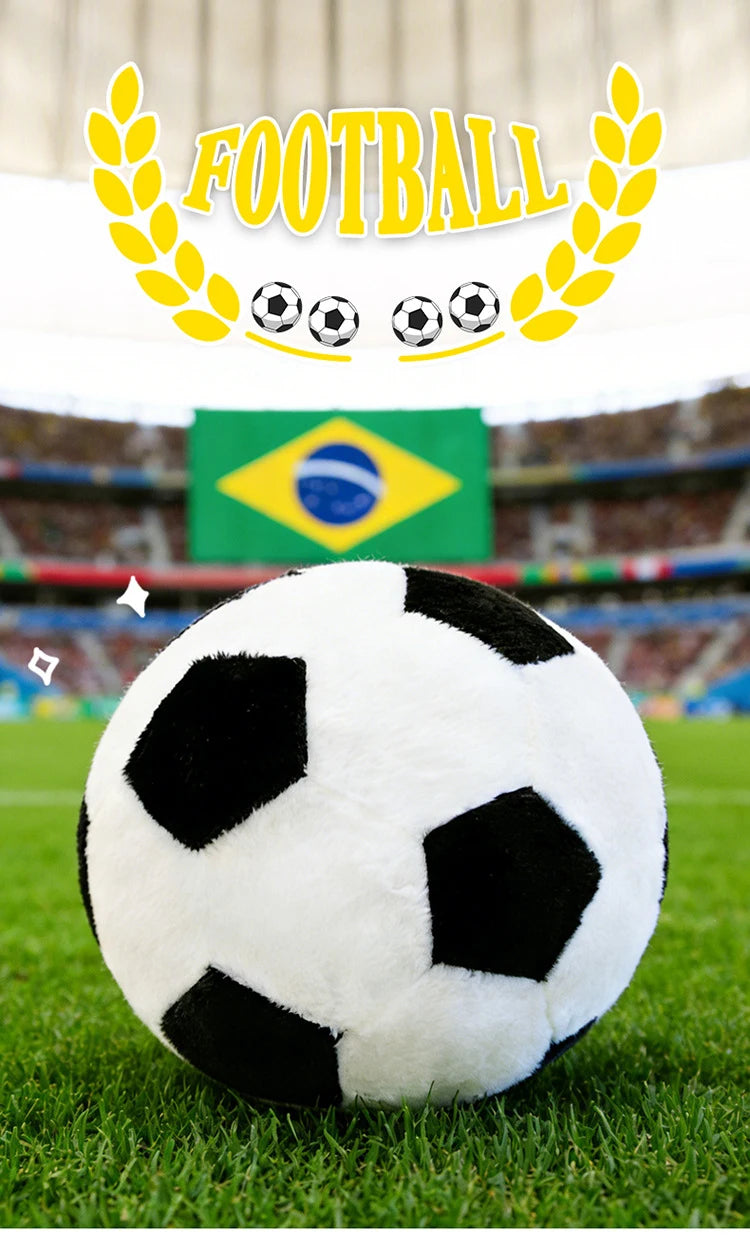 A white and black realistic football plush pillow is centered on green grass with a Brazilian flag in the background.