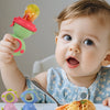 A baby is holding a green fruit feeder designed like a dinosaur, demonstrating the dripping juice feature.