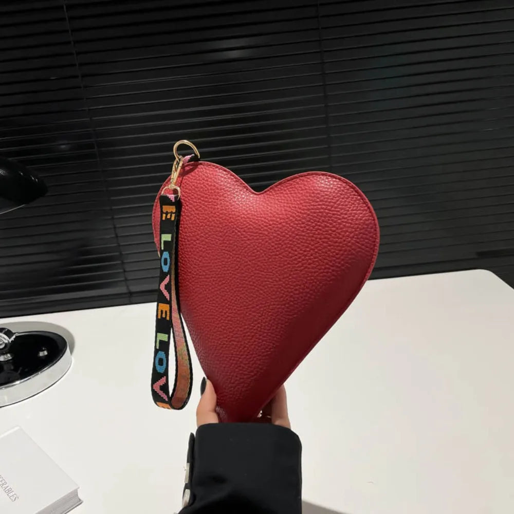 A red heart-shaped PU coin purse with a black strap is held against a dark background.