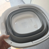A hand is holding a white collapsible bucket with multiple gray nested layers.