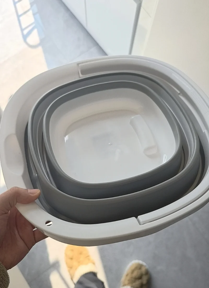 A hand is holding a white collapsible bucket with multiple gray nested layers.
