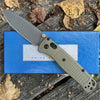 A folding pocket knife with a drop point blade and a textured handle is shown resting on a blue surface amidst dry leaves.