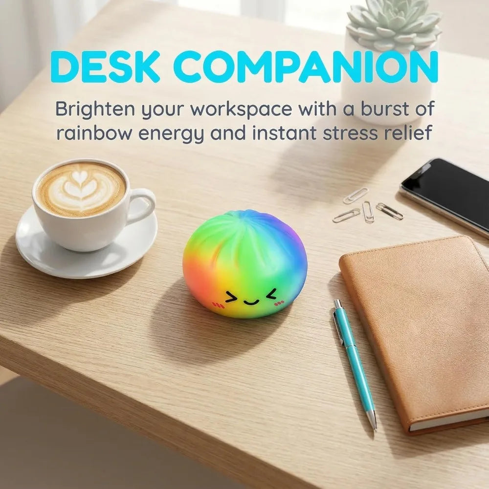 A colorful, spherical rainbow squishy toy resting on a wooden desk next to a coffee cup and notebook.