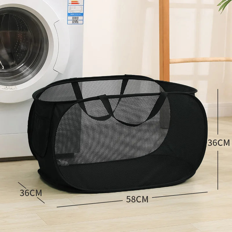 Black folding mesh laundry basket with handles shown on a wooden floor.