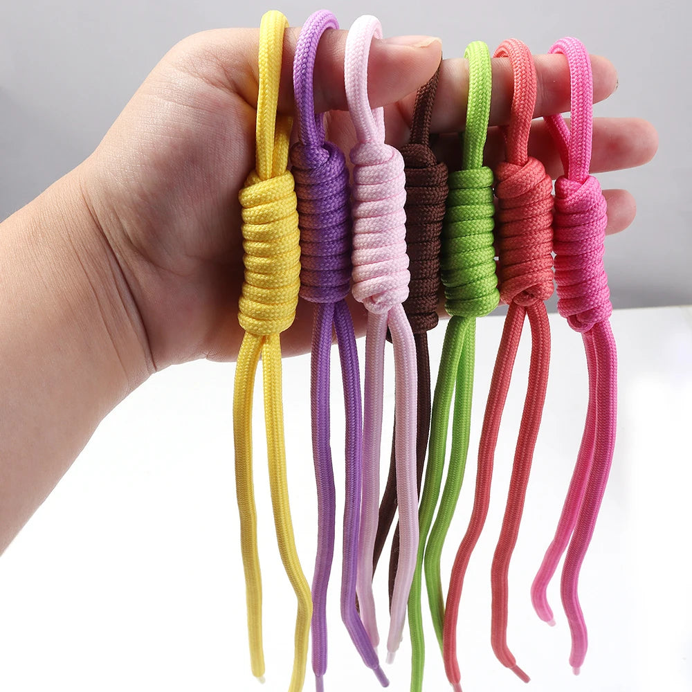A hand holds several colorful braided nylon lanyards or keychains in various shades of yellow, purple, green, and pink.