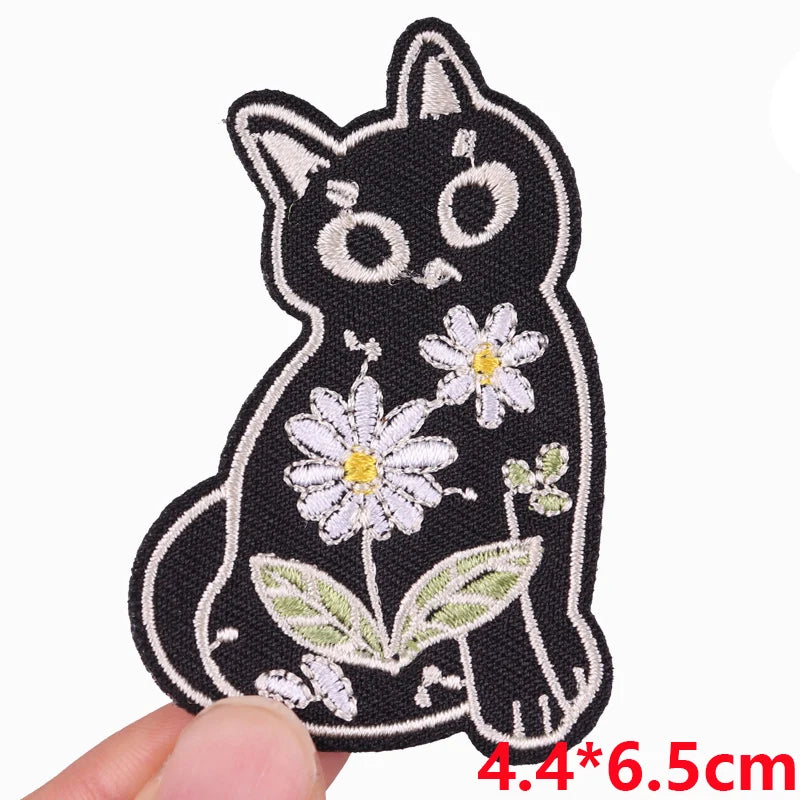 Black embroidered cat patch with white floral details on a finger