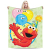 A person is holding a green Sesame Street Friends flannel throw blanket featuring a smiling orange monster character.