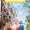 A hand holds a camera-shaped automatic bubble machine filled with numerous bubbles and lights outdoors.