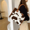 A woman holds a brown faux fur leopard print tote bag in a light indoor setting.