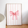 A framed canvas print featuring pink and white vertical stripes with a large pink bow design.