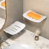 A white wall-mounted soap dish with an orange bar is displayed on a marble countertop.