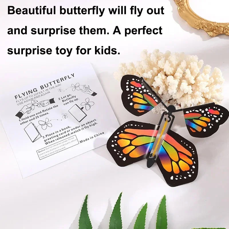 A black and orange magic flying butterfly wind-up toy is displayed next to a fluffy white pom-pom.