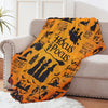 An orange Halloween flannel throw blanket with black witch and spooky designs draped over a light gray sofa.
