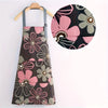 A floral print kitchen apron featuring pink, gray, and black flowers with an adjustable neck strap.