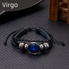 A black leather wrap bracelet featuring a blue gemstone charm on a dark textured surface.