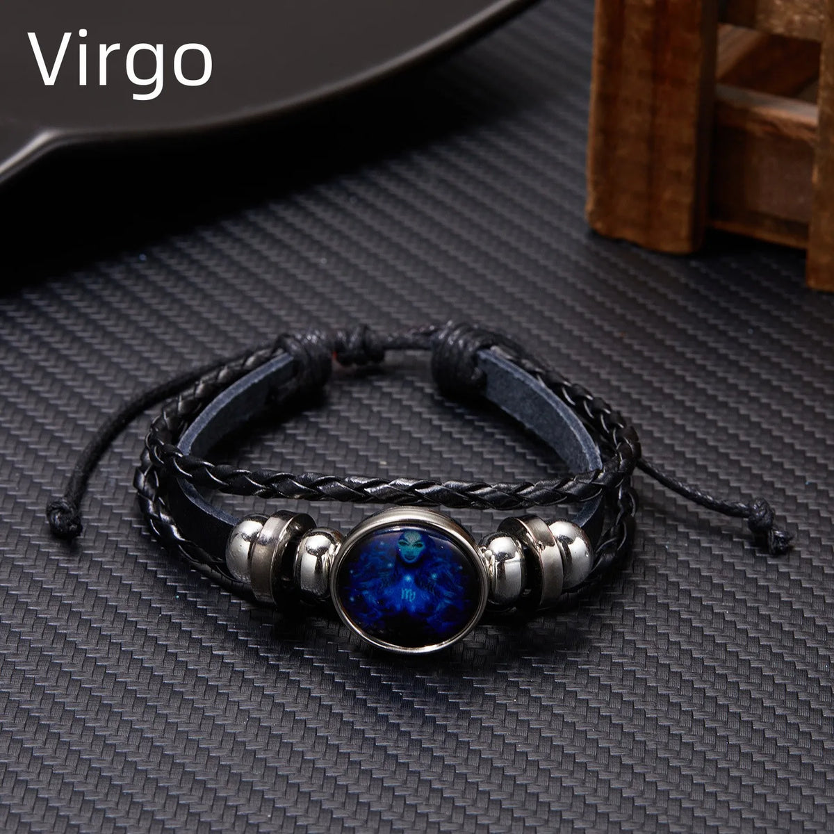 A black leather wrap bracelet featuring a blue gemstone charm on a dark textured surface.