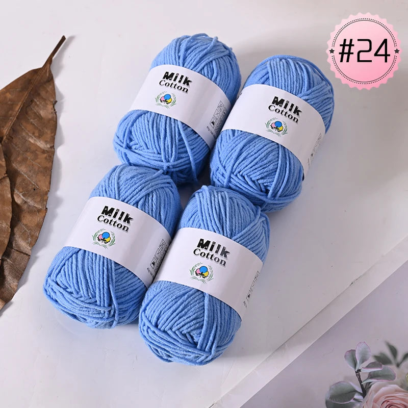 A pile of bright blue Milk Cotton yarn skeins with white labels displayed on a white surface.