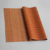 A rectangular, woven bamboo tea mat in a warm orange-brown color is shown rolled up next to its flat form.