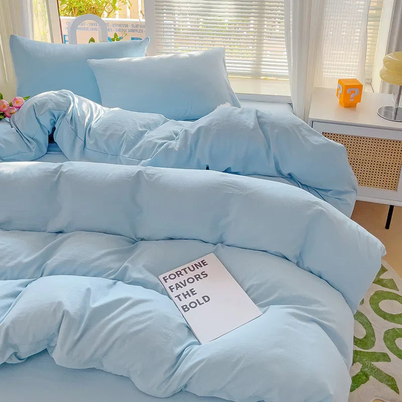 A light blue cotton bedding set featuring a flat sheet, duvet cover, and pillowcases displayed on a bed.