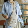 A light beige PU leather crossbody bag with a woven strap worn by a person in a blue striped shirt.