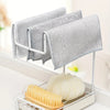 A set of ten reusable steel wire scrubber dishcloths hanging on a white rack next to a yellow brush and a white squash.