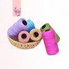 A collection of colorful 3-ply polyester knitting yarn spools in shades of purple, blue, pink, and green resting in a woven b