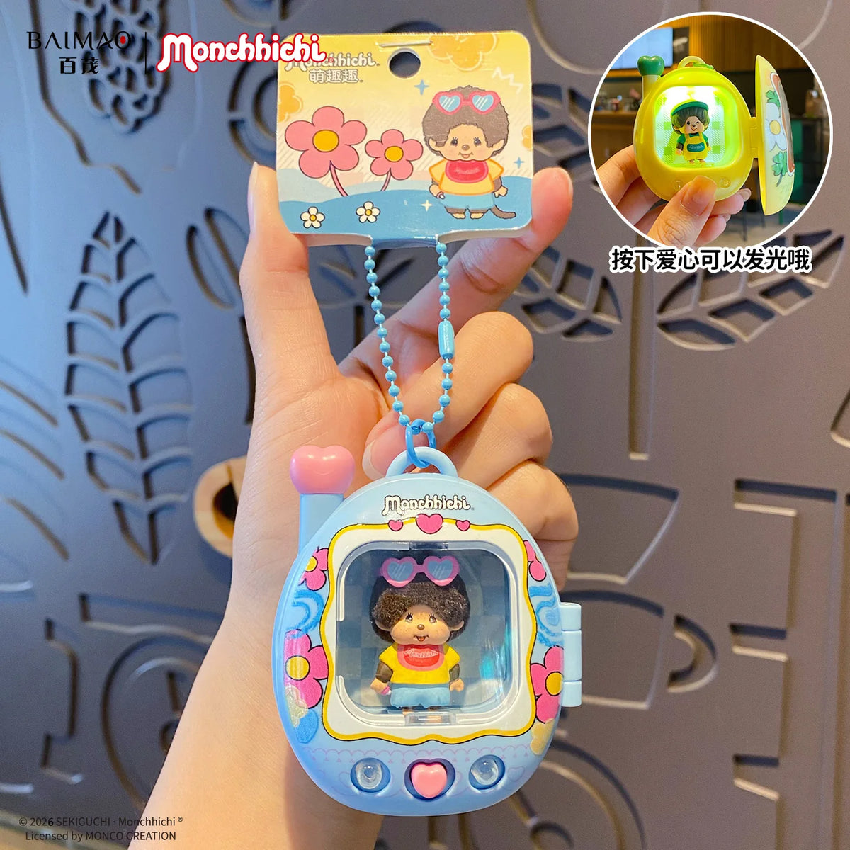 Une main tient un porte-clés de sac à dos de dessin animé avec une fonction lumineuse, représentant un personnage et des fleu