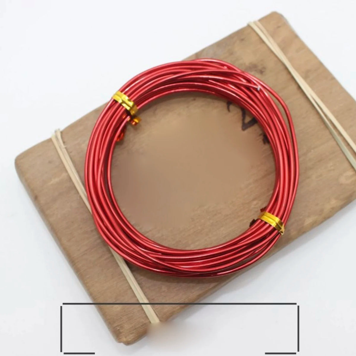 A coil of red anodized aluminum jewelry wire resting on a wooden board.