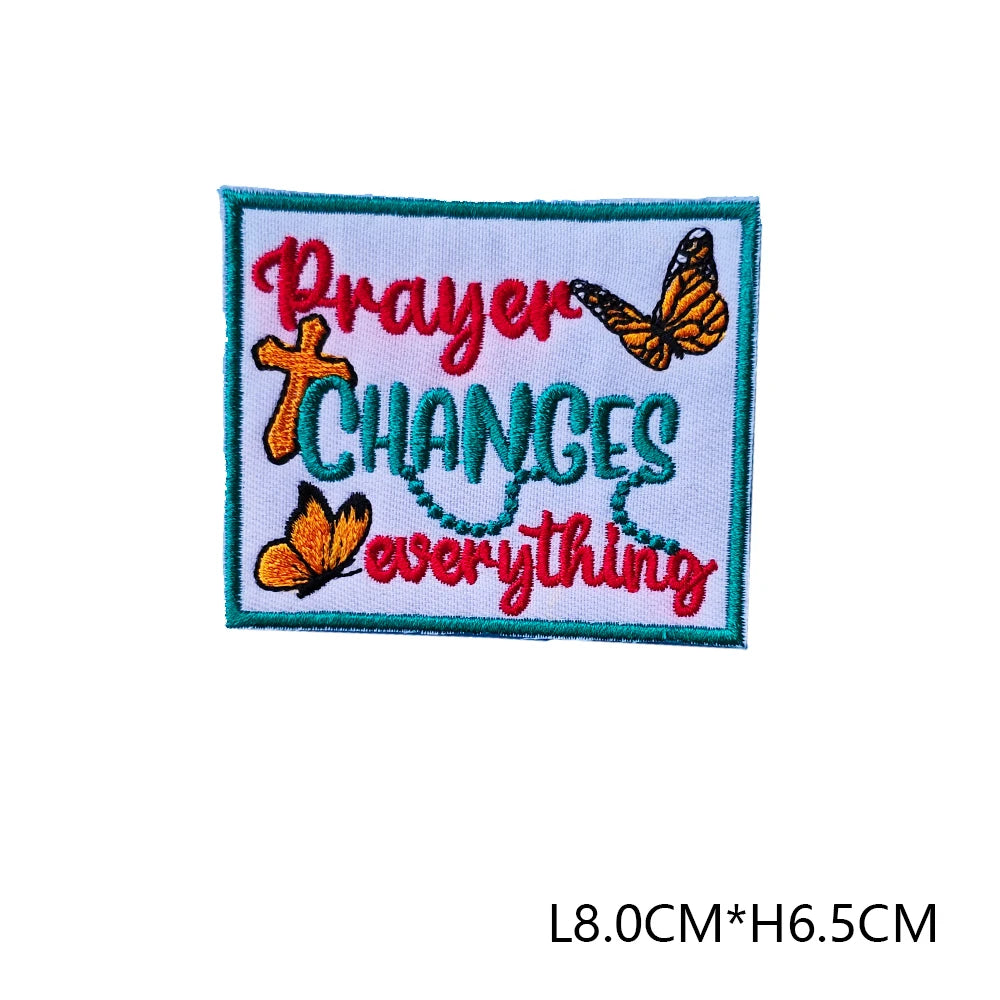 An embroidered letter patch featuring the text Prayer Changes Everything with a cross and butterfly design.