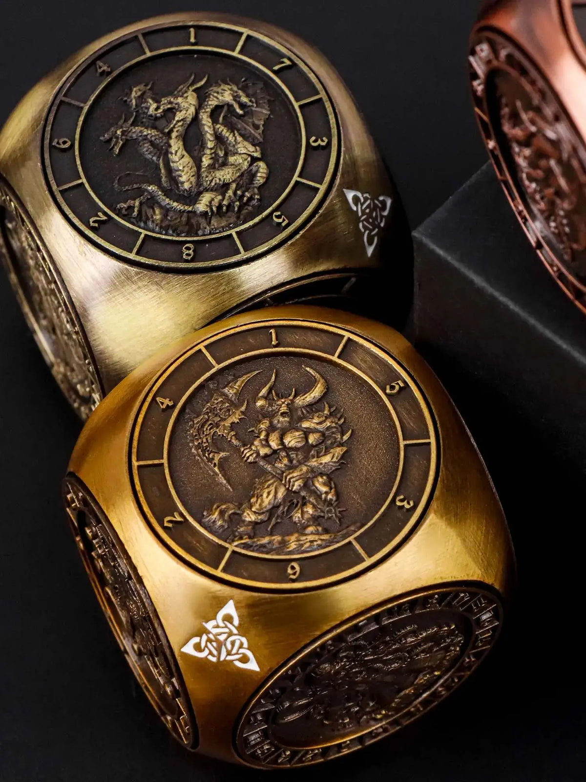 A pair of gold metal spinner dice cubes for Dungeons and Dragons displayed on a dark surface.
