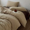 Beige, faltige Bettwäsche-Decke und Kissen mit einer kleinen braunen Tasse auf einem Bett.