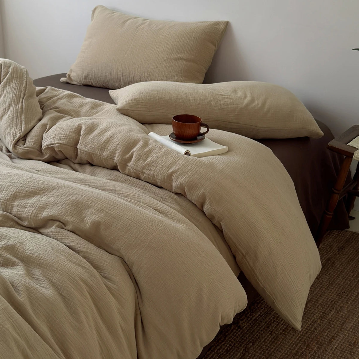 Beige, faltige Bettwäsche-Decke und Kissen mit einer kleinen braunen Tasse auf einem Bett.