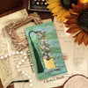 A vintage metal bookmark with an artistic hollow design and a dark green tassel resting on aged paper.