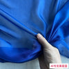 A hand is holding a piece of bright blue sheer silk chiffon fabric, showcasing its lightweight and translucent texture.