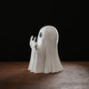 A white resin statue of a ghost with arms outstretched and a middle finger, displayed on a dark wooden surface.