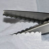 Close-up view of professional scalloped lace scissors with silver blades resting on white fabric.