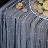 A gray tulle table runner adorned with small pearls and wooden slices, featuring a decorative silver serving dish.