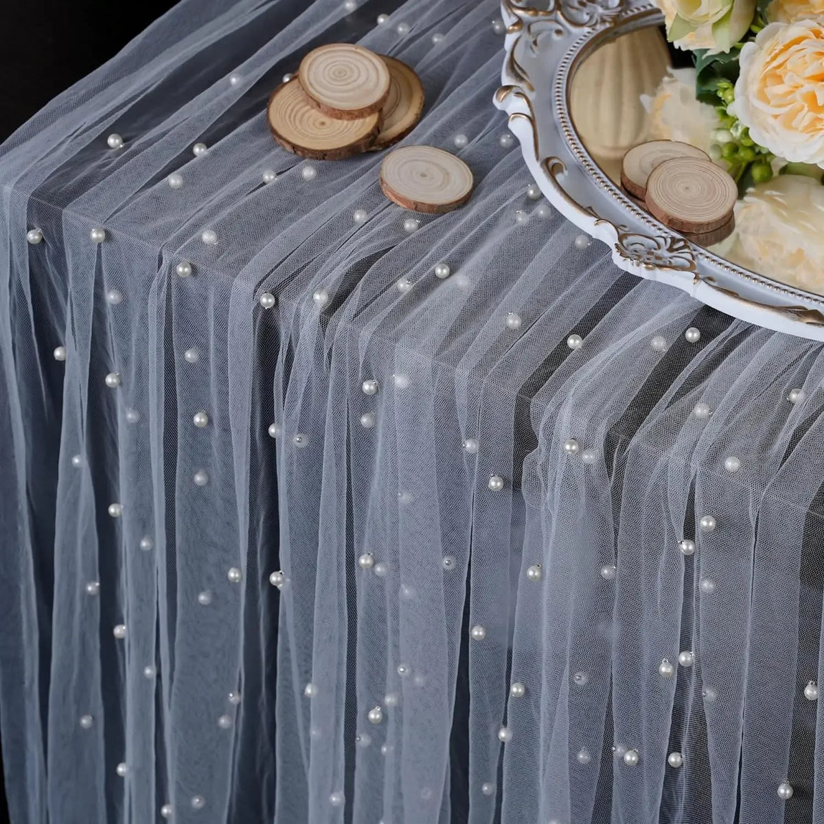 A gray tulle table runner adorned with small pearls and wooden slices, featuring a decorative silver serving dish.