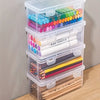 A stack of clear plastic storage boxes with lids containing various colored pencils and pens.