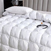 A luxurious white goose down quilt with quilted patterns is displayed on a bed.