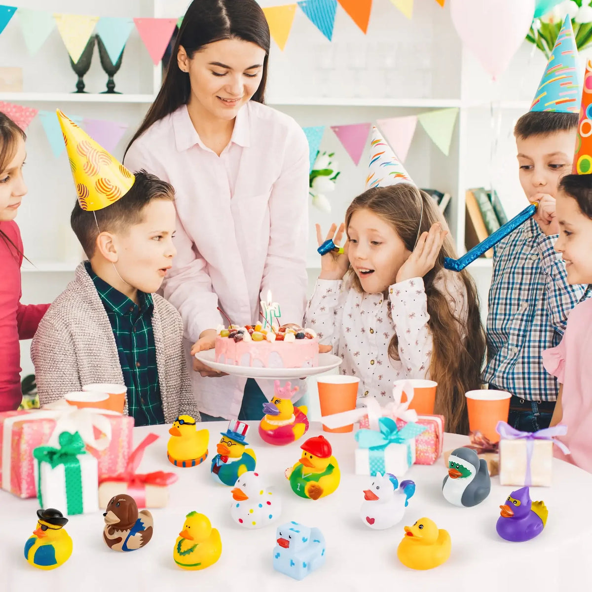 A variety pack of colorful mini rubber ducks and related toys displayed on a white table with children.
