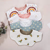 A collection of five white muslin cotton baby bibs and burp cloths featuring various patterns including rainbows, florals, an